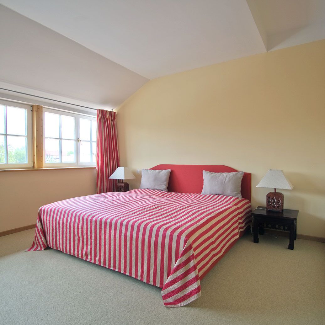 A bedroom with a bed, two bedside tables, a window with curtains, and a view outside.