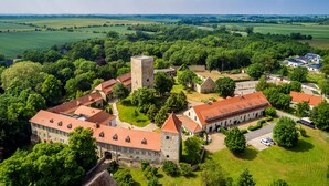 An aerial view of a historic building complex with a central tower, surrounded by lush greenery and fields. - Hotel Burg Wanzleben (Wanzleben-Börde)