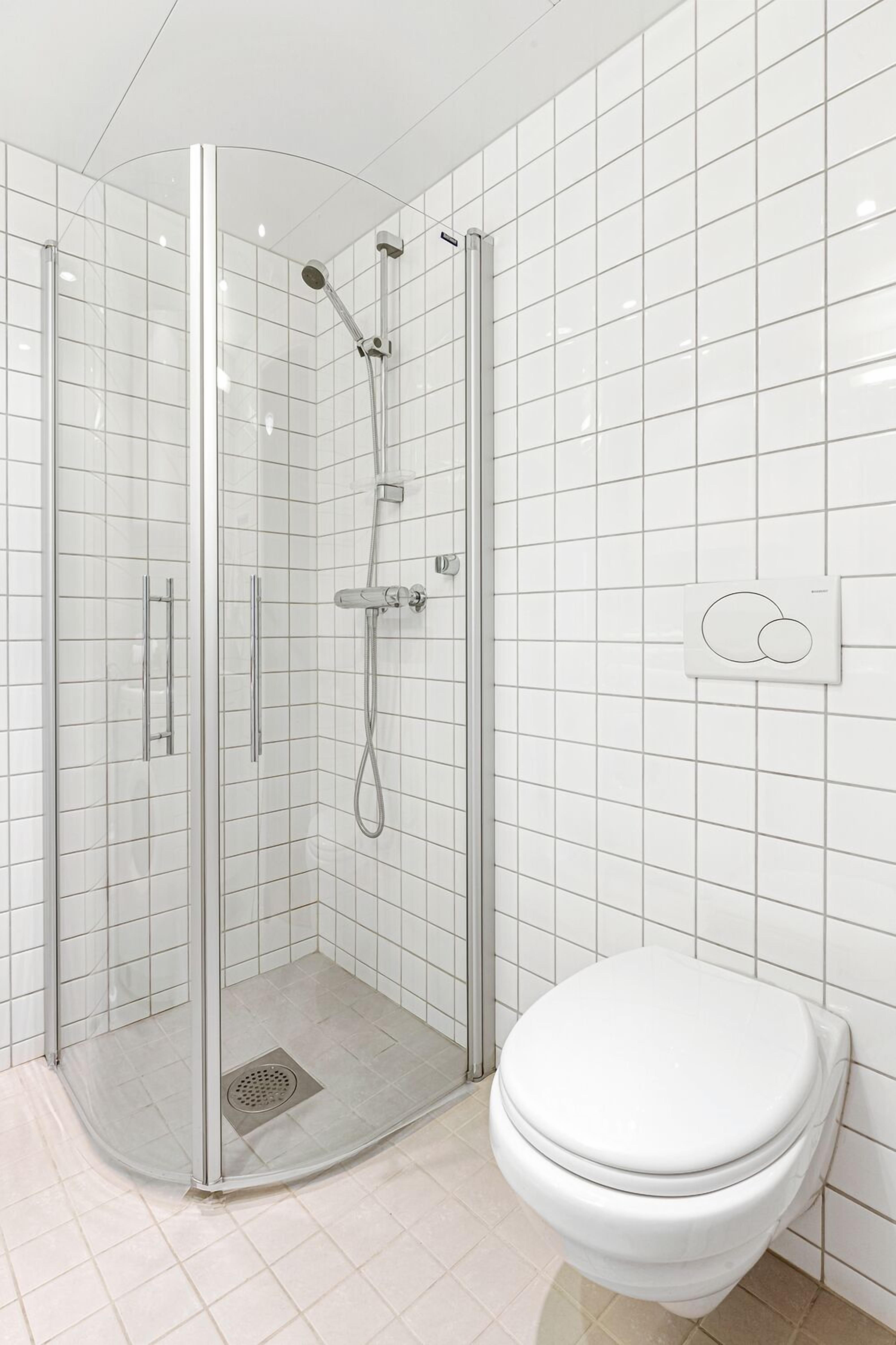 A modern bathroom with a glass-enclosed shower, a white toilet, and a tiled wall.