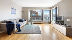 A modern living room with a sofa, a glass coffee table, a TV, and a view of the city through large windows. - BJØRVIKA APARTMENTS, Teaterplassen, Oslo city center (Oslo)