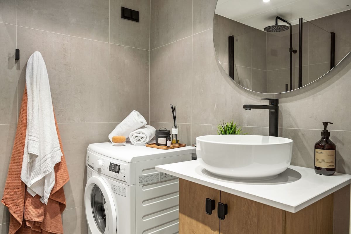 Une salle de bain moderne équipée d’un lave-linge, d’un grand lavabo et d’un miroir.