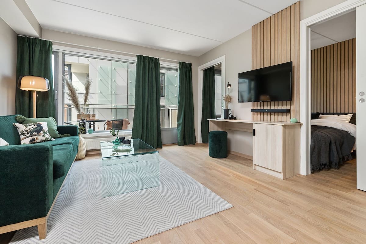 Un salon moderne avec un canapé vert, une table basse en verre et un téléviseur fixé au mur.