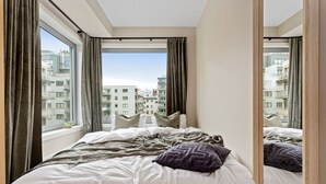 A bedroom with a large bed, a view of the city through the window, and a mirror reflecting the room. - BJØRVIKA APARTMENTS, Teaterplassen, Oslo city center (Oslo)