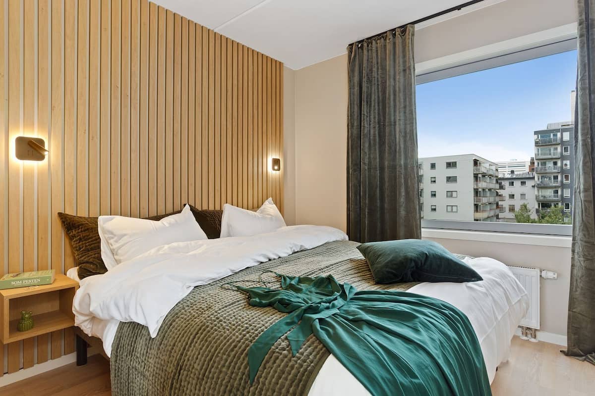 Une chambre d’hôtel moderne avec un grand lit, un mur lambrissé en bois et une vue sur le paysage urbain.