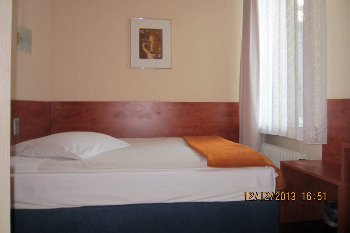 A hotel room with a single bed, a headboard, a framed picture on the wall, and a window with curtains.