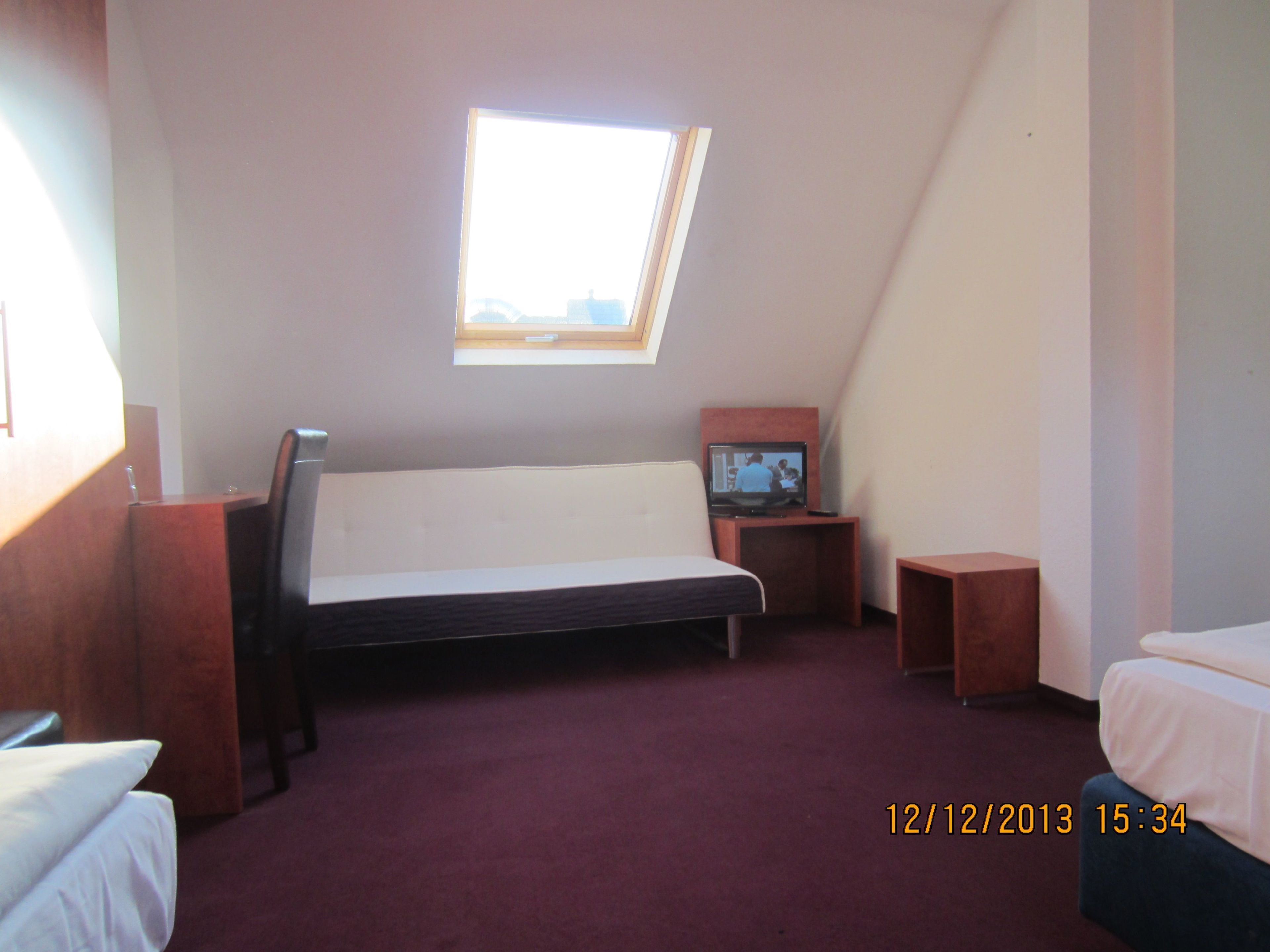 A small, single-room apartment with a sloped ceiling, a skylight, a bed, a desk, and a television.
