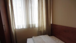 Ein Hotelzimmer mit Bett, einem Fenster mit durchsichtigen Vorhängen und einem Holzkopfteil.