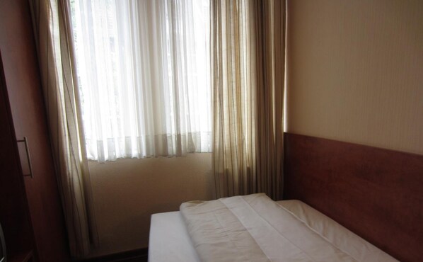 A hotel room with a bed, a window with sheer curtains, and a wooden headboard. - Hotel Haus Rheinblick (Düsseldorf)