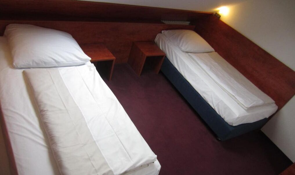 Una habitación con dos camas individuales, cada una con ropa blanca y almohadas, y una mesita de noche de madera entre ellas.