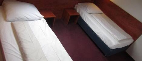 Una habitación con dos camas individuales, cada una con ropa blanca y almohadas, y una mesita de noche de madera entre ellas.