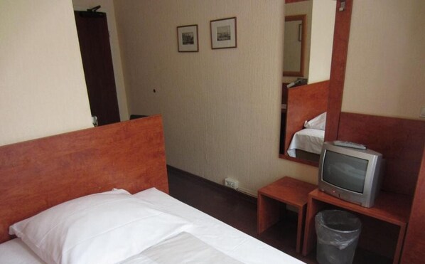 A hotel room with a single bed, a small bedside table with a television, a mirror, and two framed pictures on the wall.