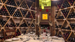 A wine cellar with wooden racks filled with bottles, a table set for dining, and a lit candle. - Al Posta Hotel 1899 (Baselga di Pine)