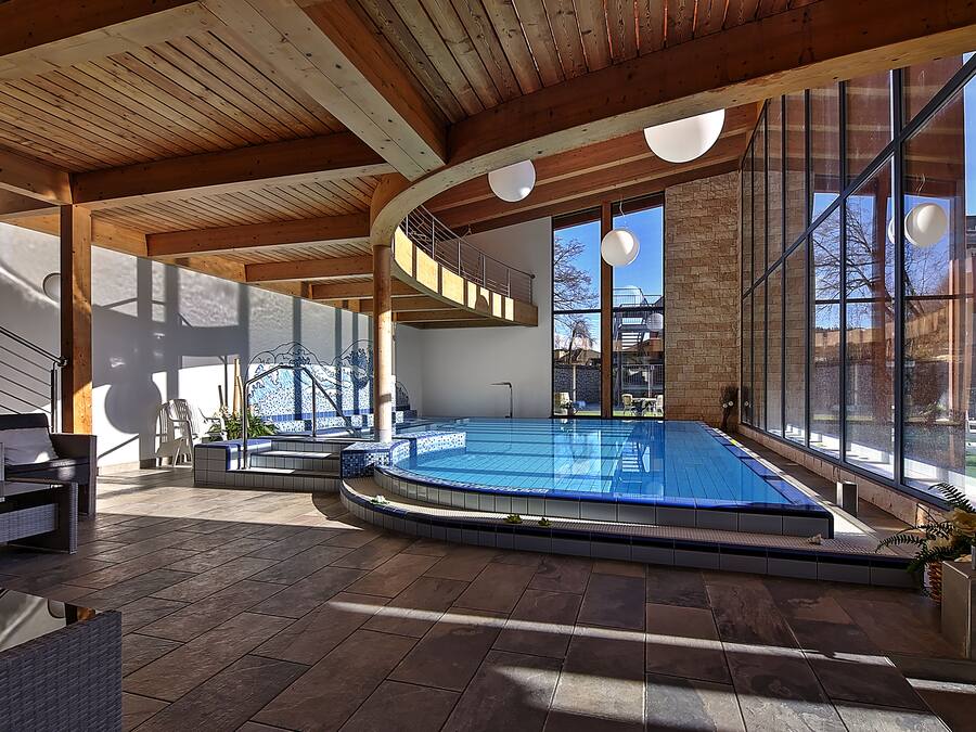 Ein moderner, überdachter Schwimmbereich mit Holzbalkendecke und großen Fenstern.