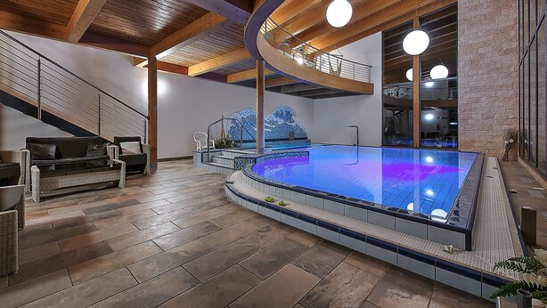 A spacious indoor swimming pool with a tiled edge, wooden ceiling beams, and a staircase leading to an upper level. - Al Posta Hotel 1899 (Baselga di Pine)
