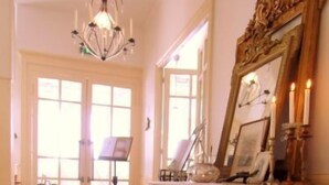 Um corredor com ladrilhos estampados, um lustre e um espelho com moldura decorativa.