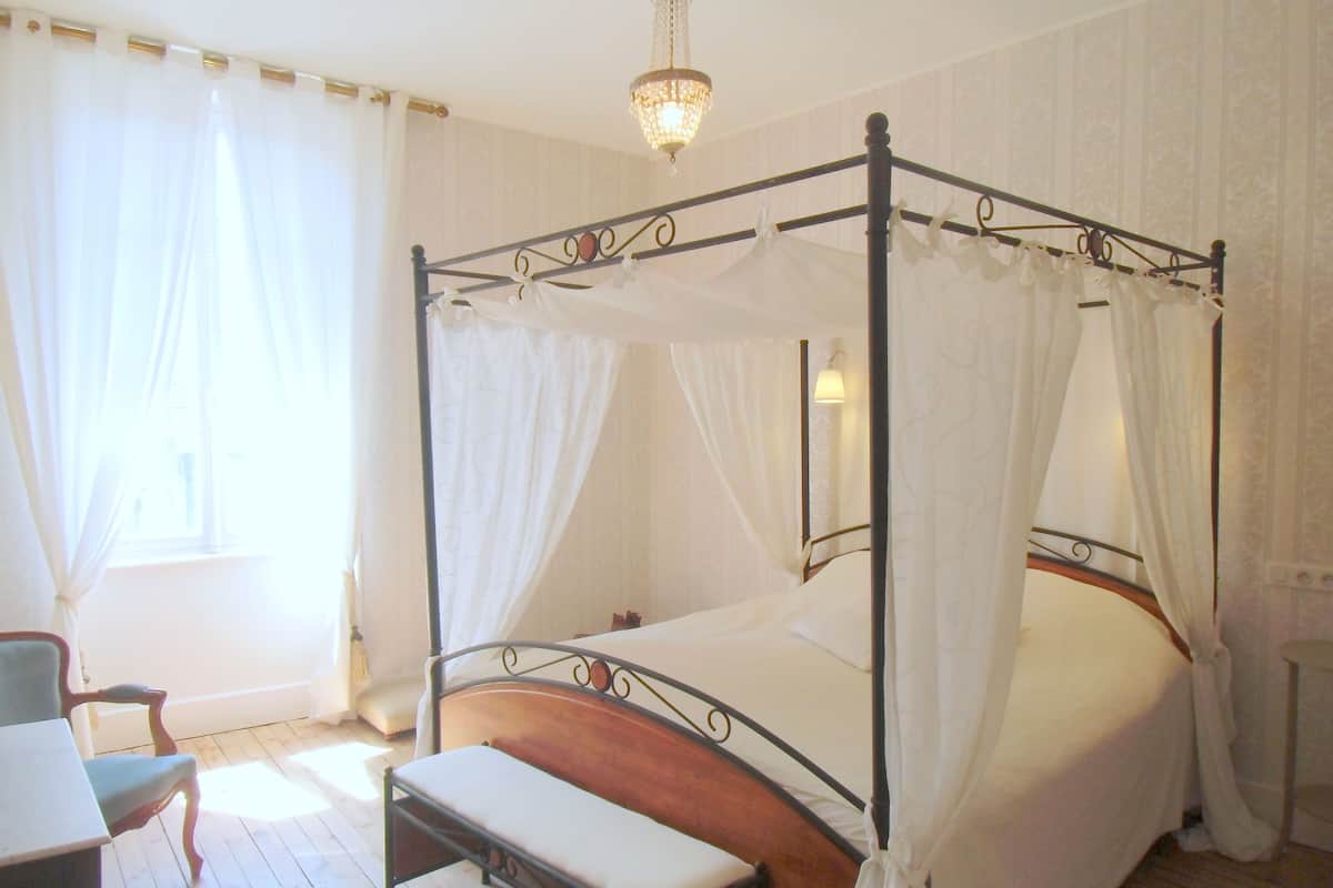 Una cama con dosel y cuatro columnas, ropa de cama blanca, un banco de madera y un candelabro.