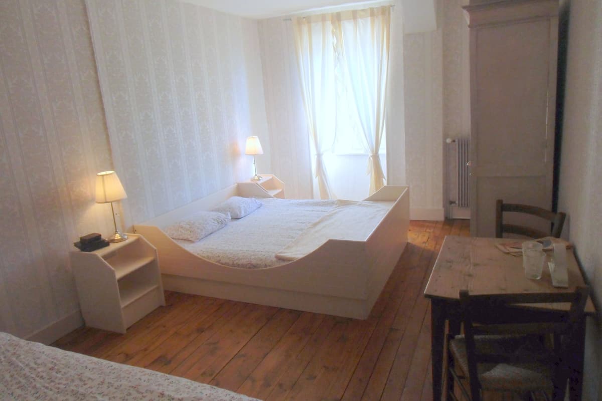 Un dormitorio con cama, mesitas de noche, lámpara, una mesa con sillas y un armario.
