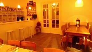 Uma sala de jantar com uma mesa de madeira comprida, banquetas de bar e um bar com prateleiras cheias de garrafas.