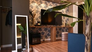Una sala de estar moderna con un televisor de pantalla plana grande, piso de madera, un sofá azul y un papel tapiz estampado.