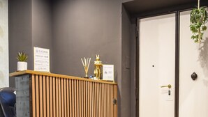 Un área de recepción con un mostrador de madera, una silla de oficina azul, una mesa redonda con una silla dorada y una planta en maceta.