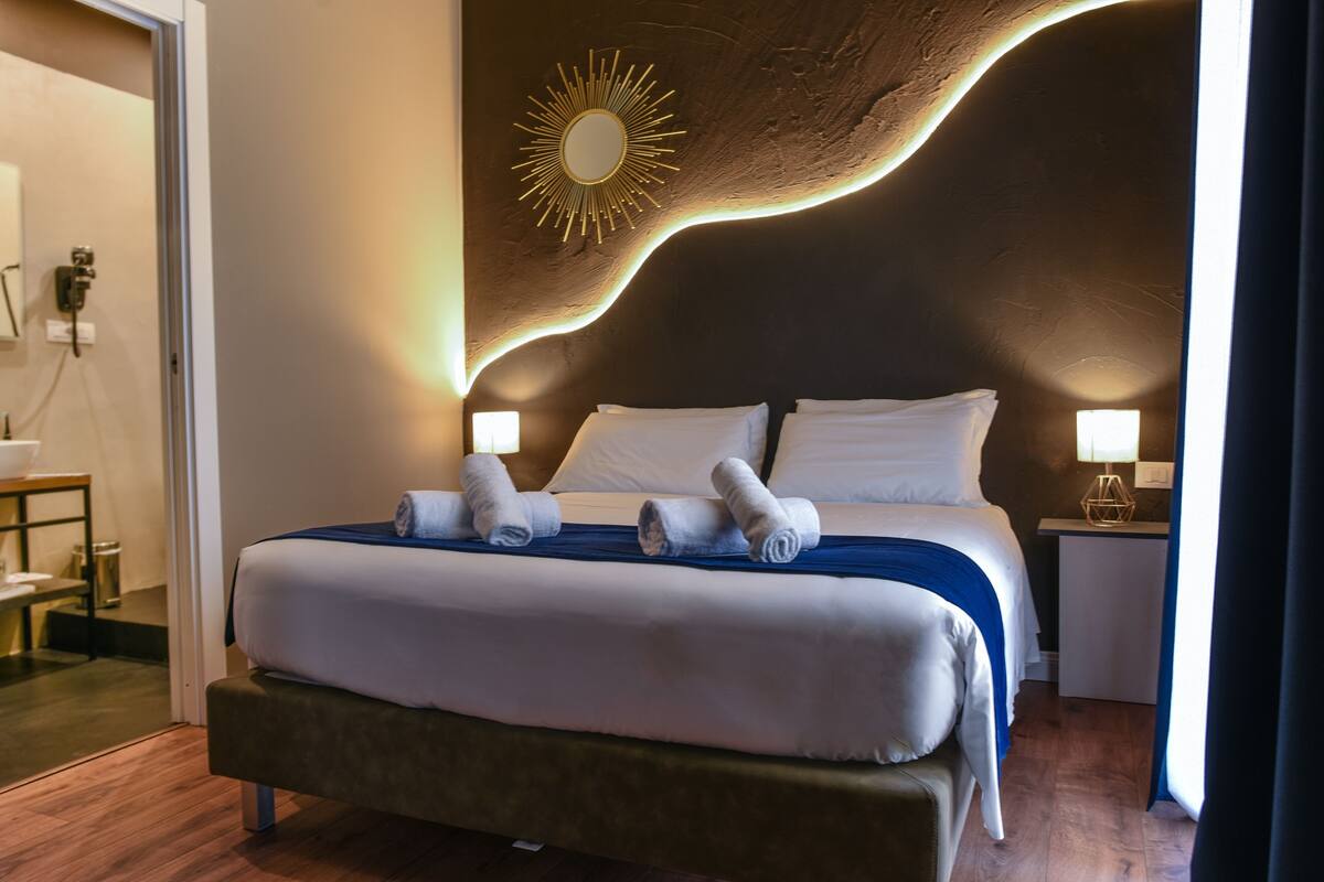 A hotel room with a large bed, two bedside tables, a wall-mounted mirror, and a unique ceiling design.