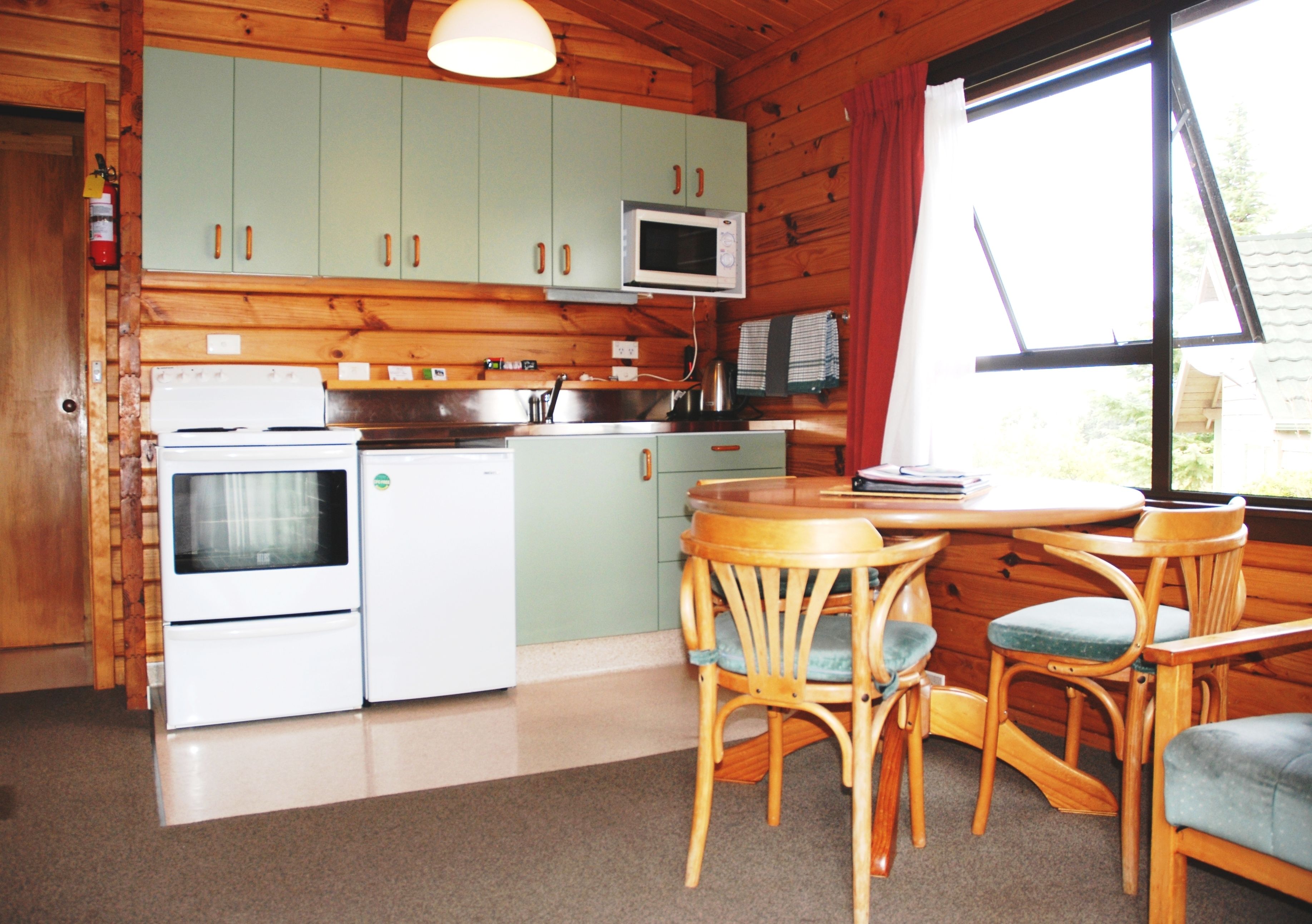 A compact kitchen with wooden cabinets, a microwave, a sink, and a dining area with wooden chairs.