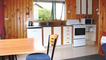 Una cocina compacta con paredes de madera, una ventana, microondas, estufa y fregadero.