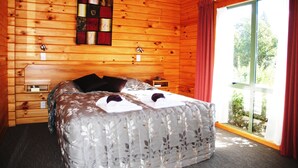 Une chambre à coucher dans un chalet en bois, avec un lit, une table de chevet, une horloge murale et une fenêtre avec des rideaux.