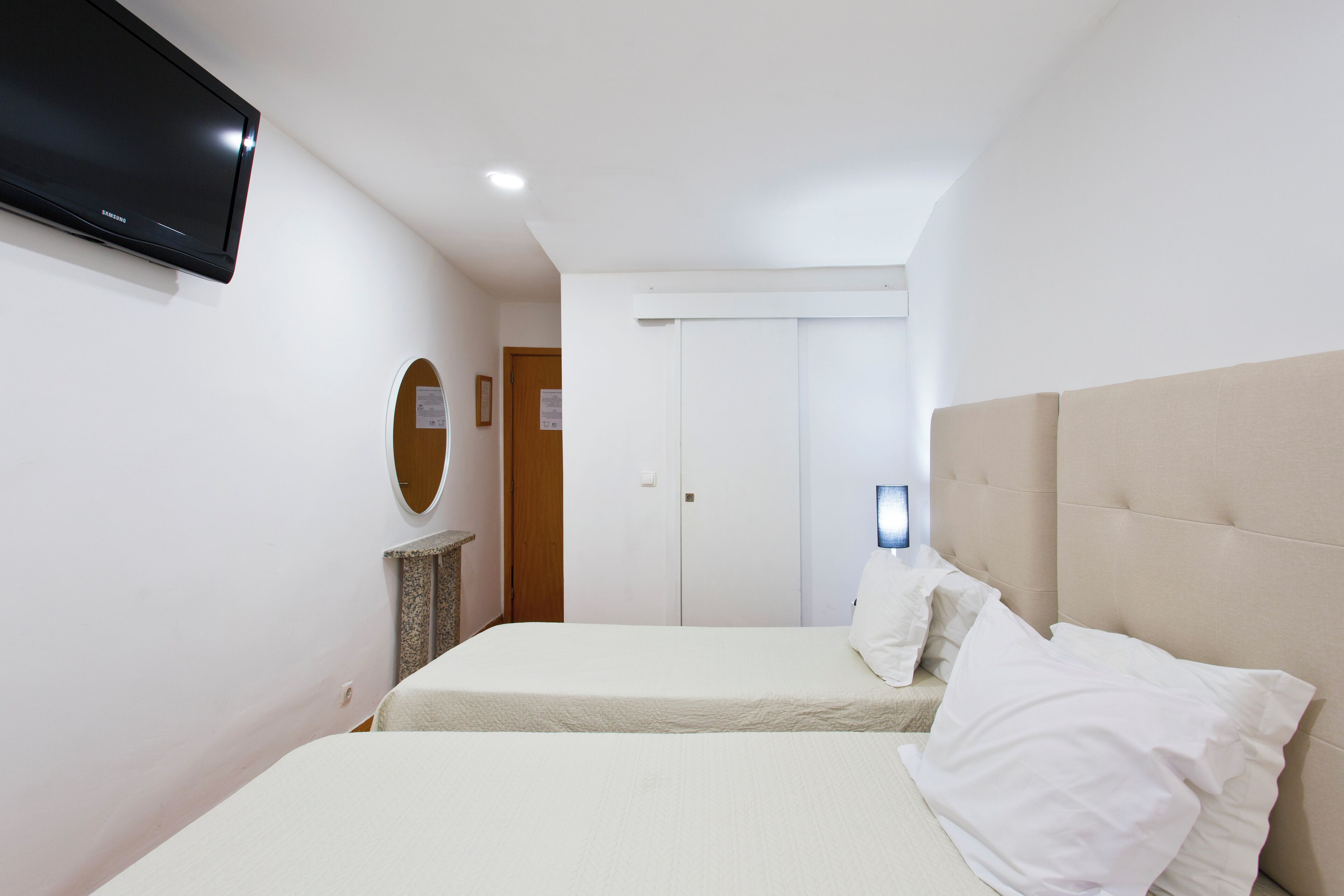 Un dormitori amb dos llits, un televisor penjat a la paret i una porta al fons.