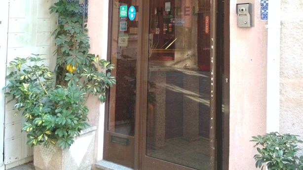 Entrada de hotel con puerta de vidrio, toldo verde y pared de azulejos.