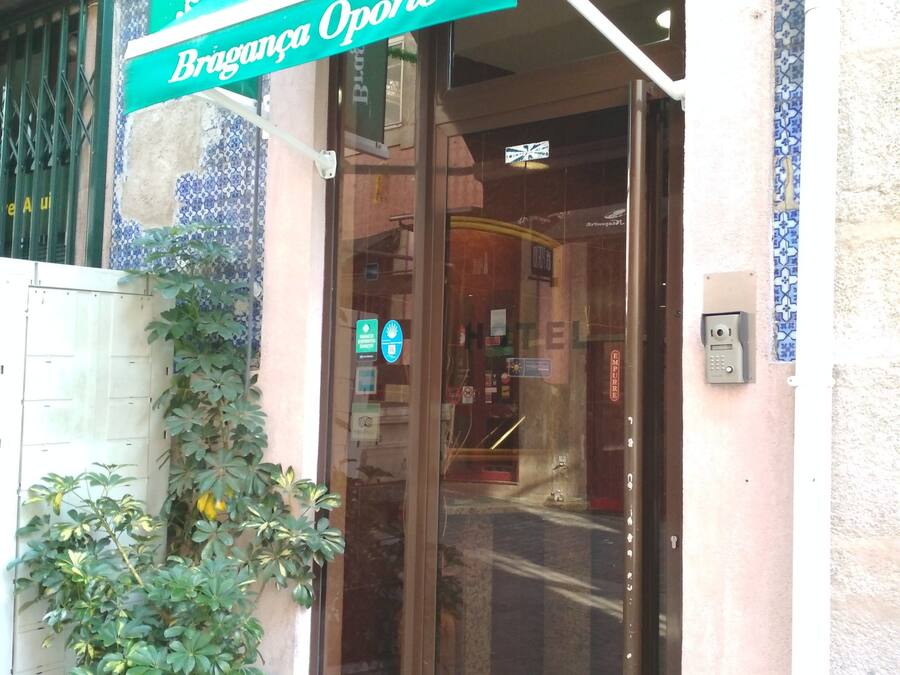 Entrada de hotel con puerta de vidrio, toldo verde y pared de azulejos.