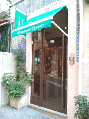 Entrada de hotel con puerta de vidrio, toldo verde y pared de azulejos.