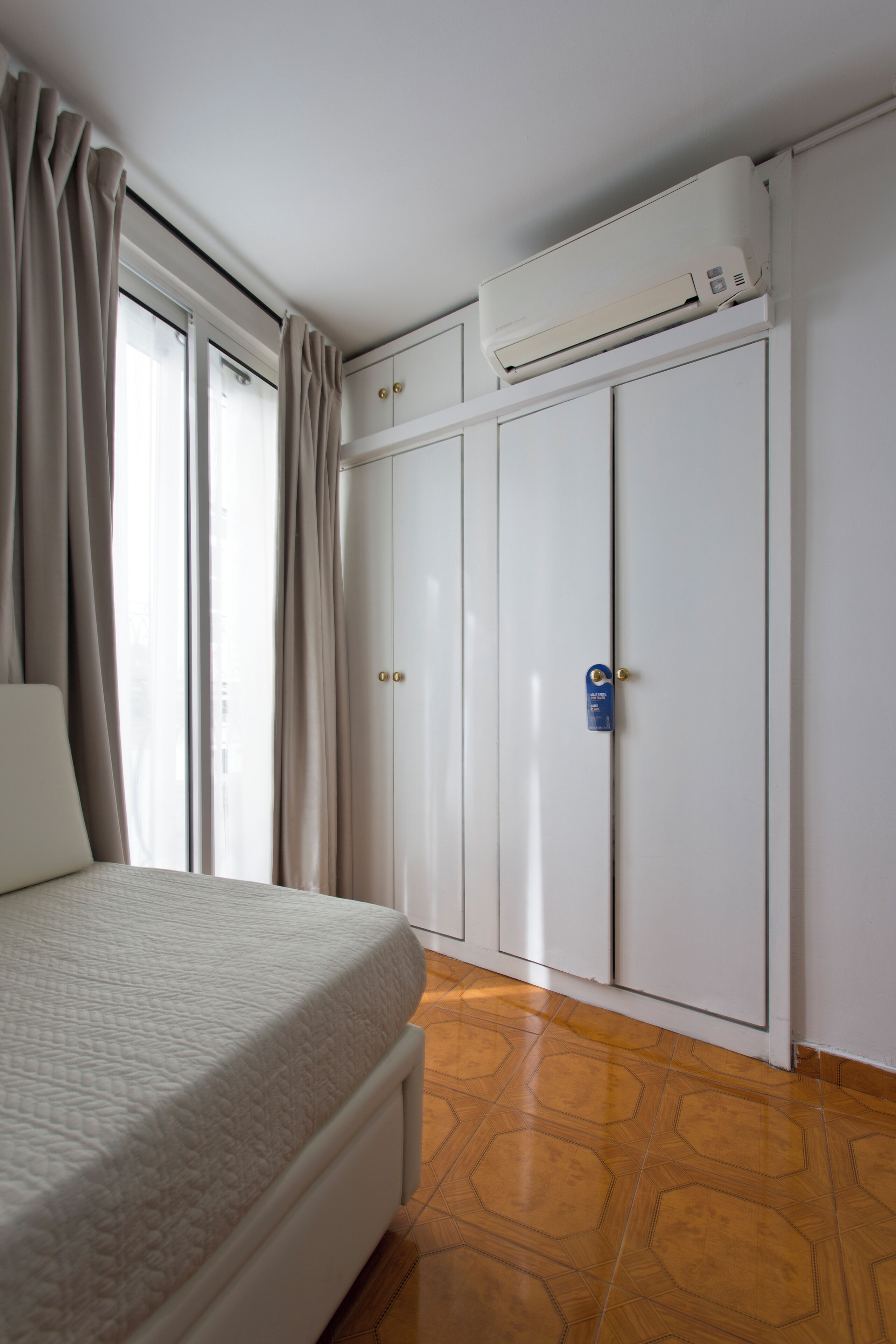 A bedroom with a bed, a wardrobe, and an air conditioning unit.