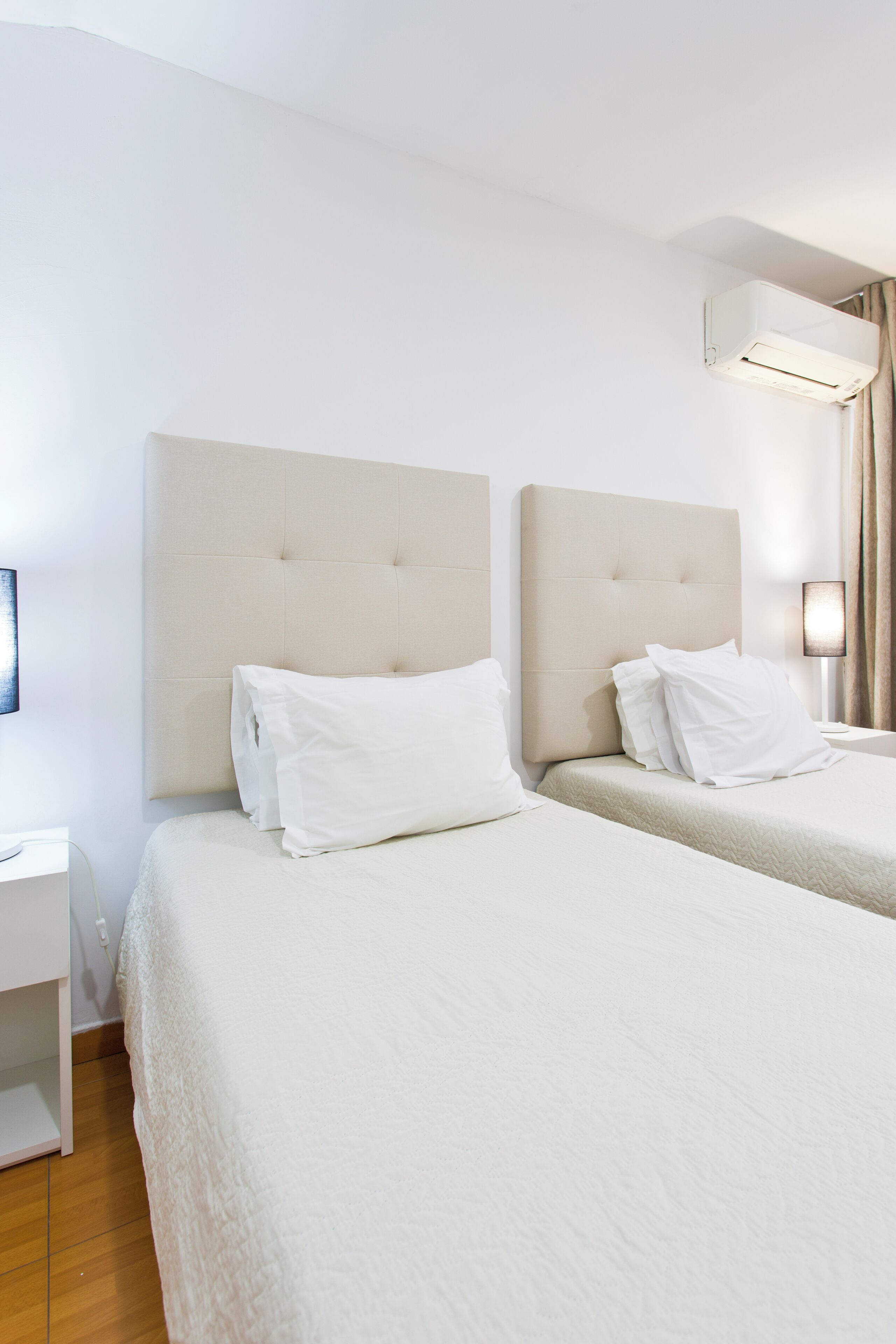 A hotel room with two beds, a nightstand, a lamp, and an air conditioning unit.