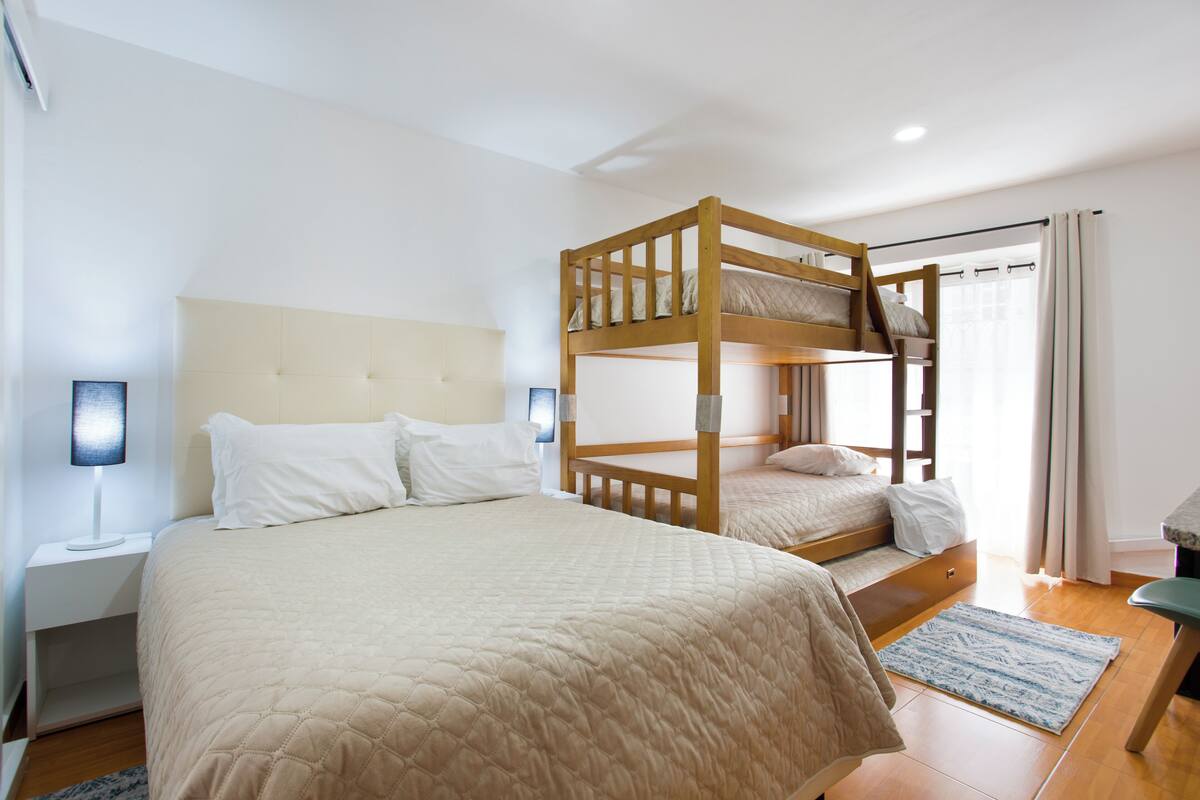 A bunk bed room with a headboard, bedside tables, and a window with curtains.