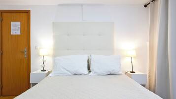 Habitación de hotel con cama, dos mesitas de noche con lámparas, una puerta de madera y cabecera blanca.