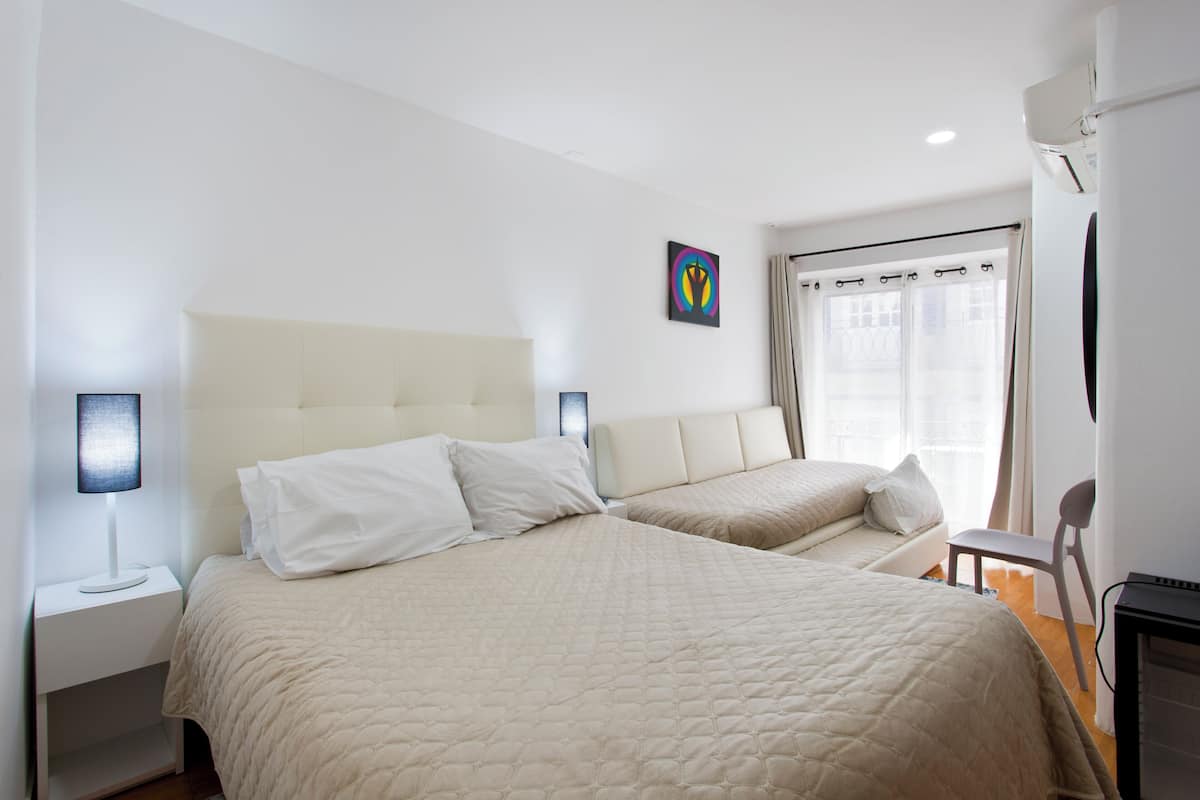 A hotel room with two beds, a bedside table with a lamp, a chair, and a TV.