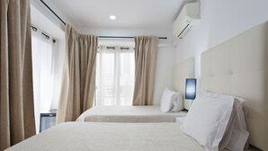 Una habitación de hotel con dos camas, cortinas color beige, un ventanal con vistas y un equipo de aire acondicionado.