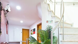 Pasillo de hotel con alfombra roja, una escalera con barandillas de metal, una planta en maceta y una puerta con número.