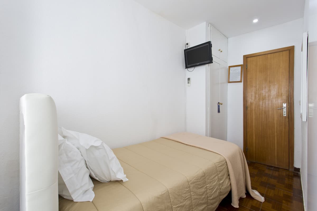 A small, clean room with a single bed, a mounted television, and a wooden door.
