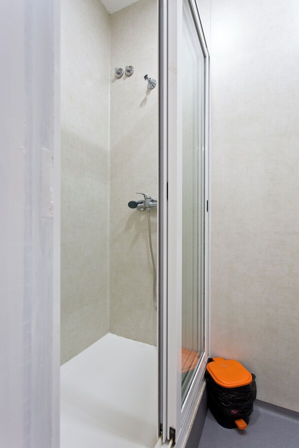 A shower area with a glass door, a bathtub, and a trash bin.