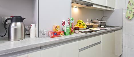 A kitchen with white cabinets, a stainless steel kettle, a toaster, and various food items on the counter.