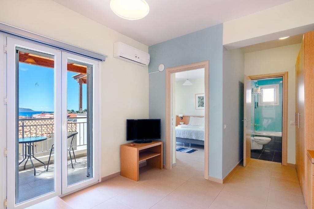 A room with a balcony, a television, a bed, and a bathroom.