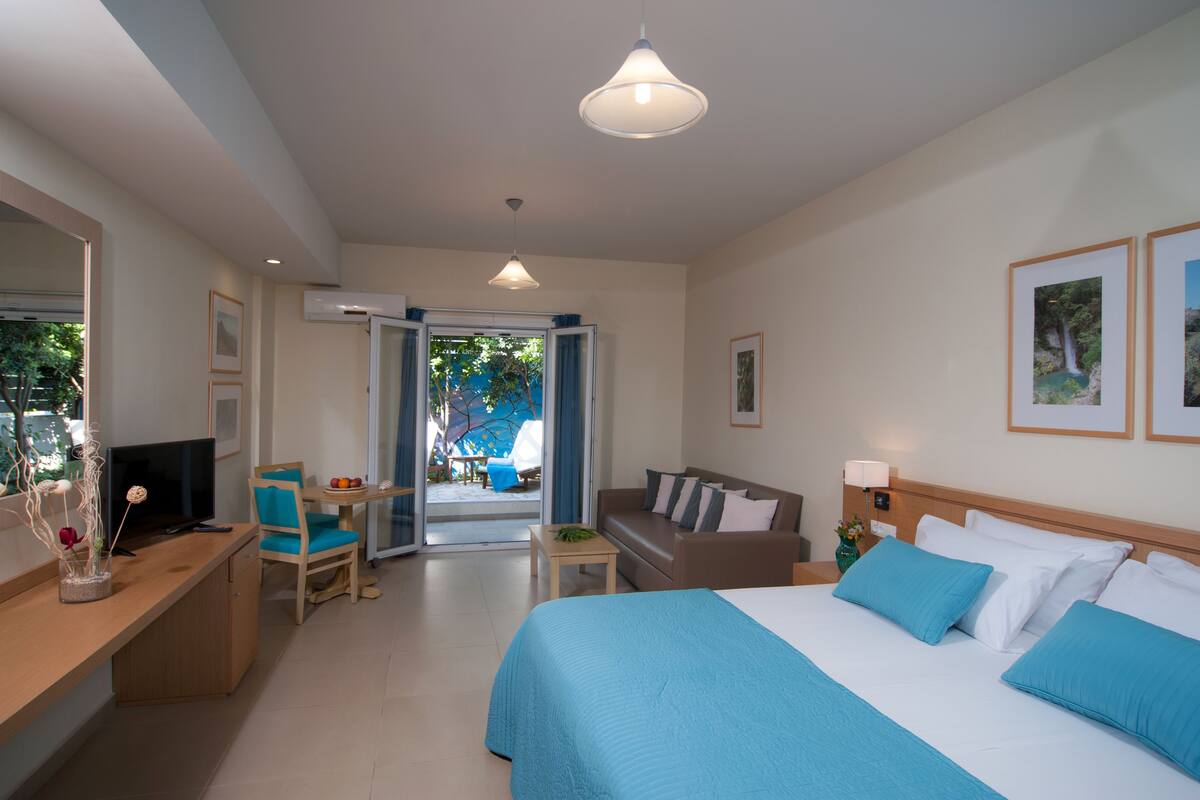 A hotel room with a bed, a desk, a TV, a chair, a small table, and a window with a view of the outdoors.