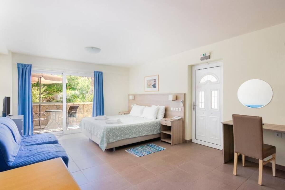 A bedroom with a bed, a desk, a chair, a TV, a door, and a window with curtains.