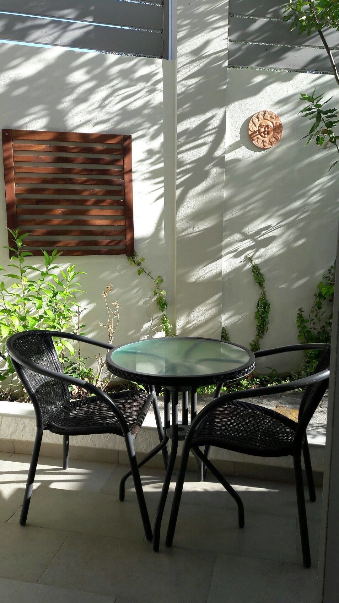 A patio with a round table and four chairs, surrounded by plants and a wooden slat window.