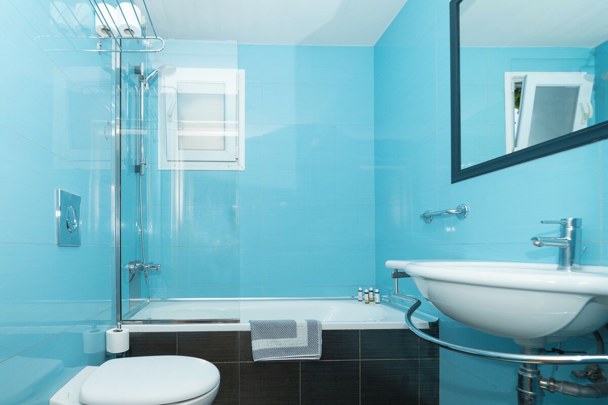 A bathroom with a glass shower enclosure, a white toilet, a bathtub, and a sink with a mirror above it.