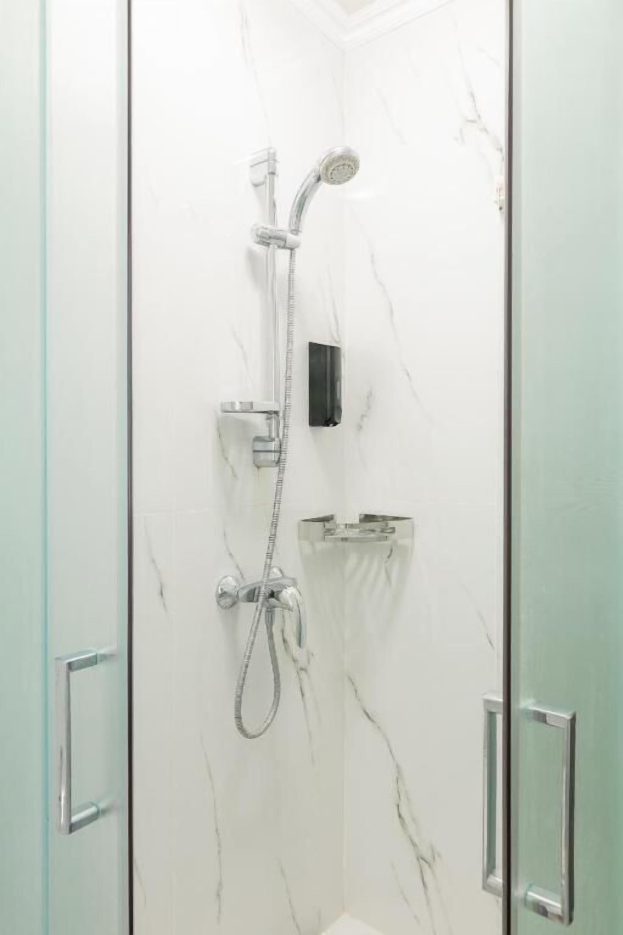 Una cabina doccia in vetro con soffione a mano e rubinetto a parete.