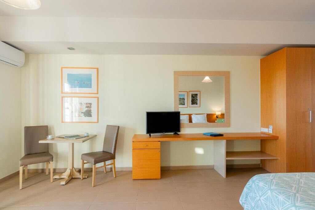 A hotel room with a bed, a desk with a computer, two chairs, a small table, and a wardrobe.
