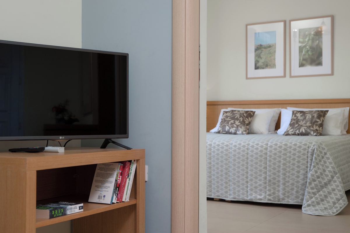 A bedroom with a bed, a TV on a wooden stand, and two framed pictures on the wall.